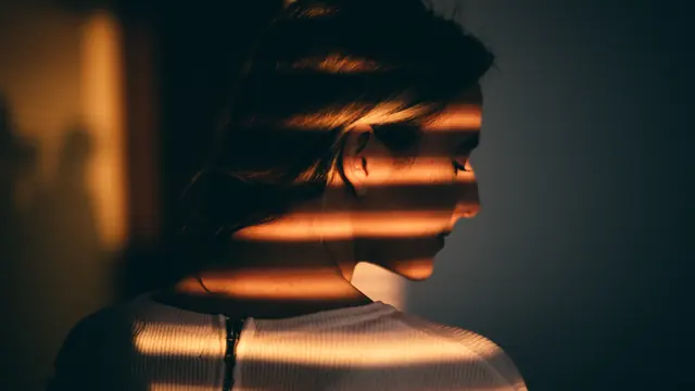 A person in alternating bands of warm light and shadow