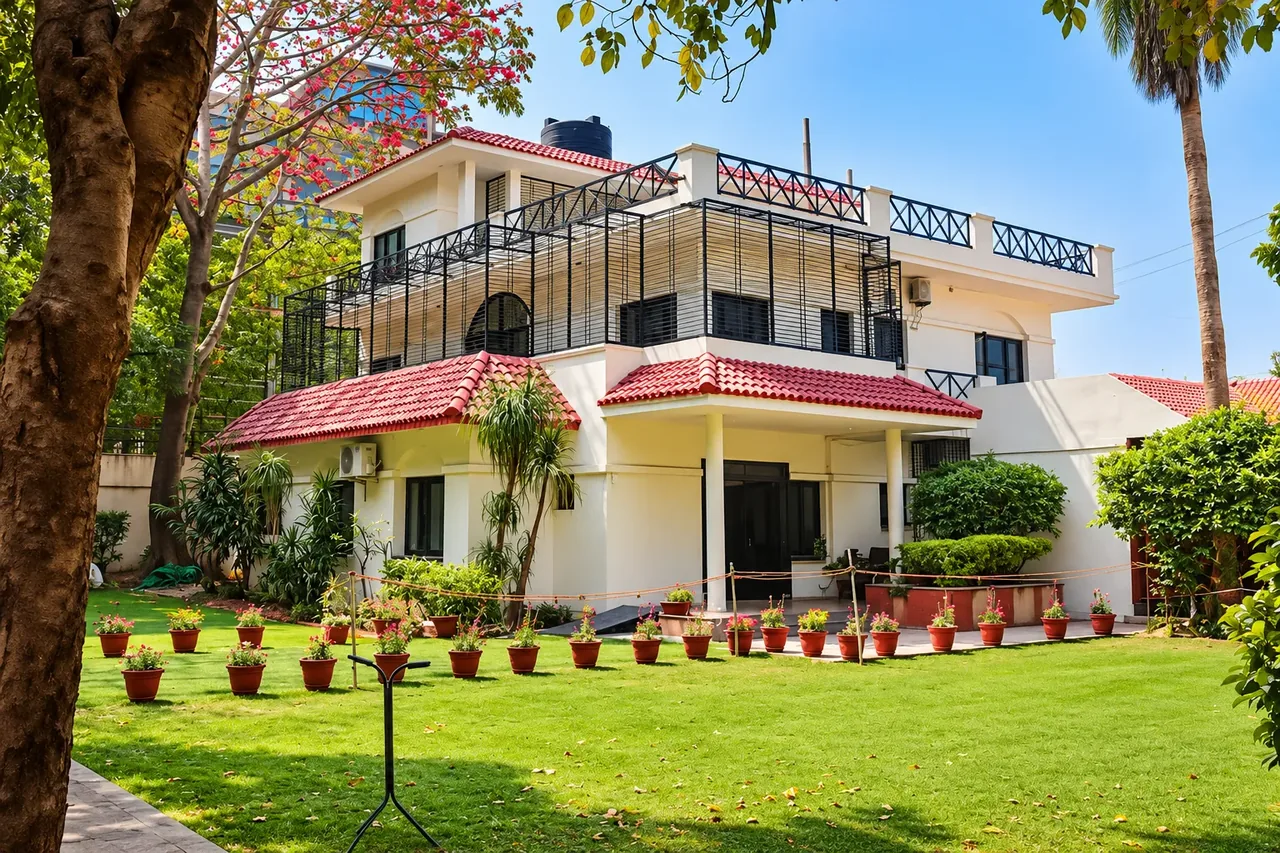 A white two-storey house with a red tiled roof and a lawn at the Mehrauli centre