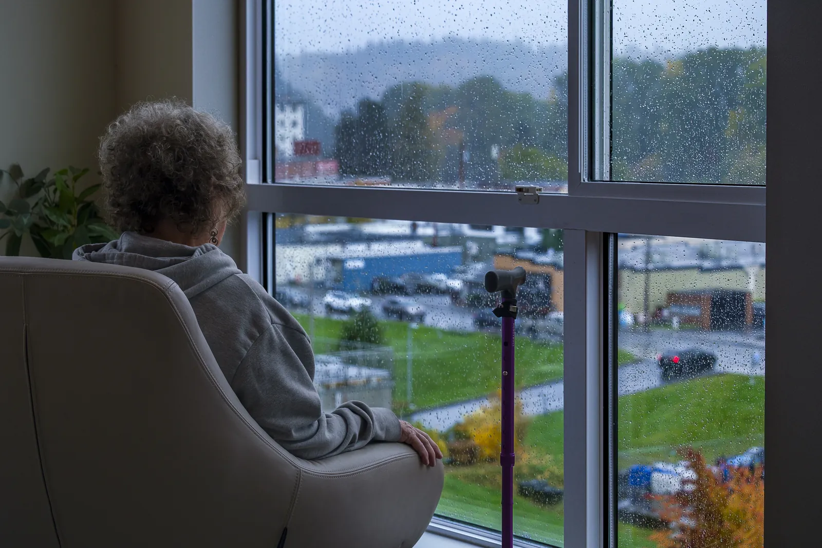 Woman sits in chair looking out rainy window